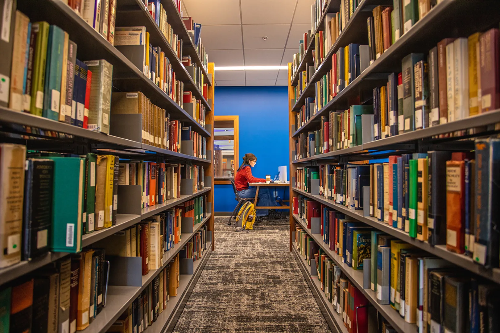 A student studying in the new library with books in the foreground. 