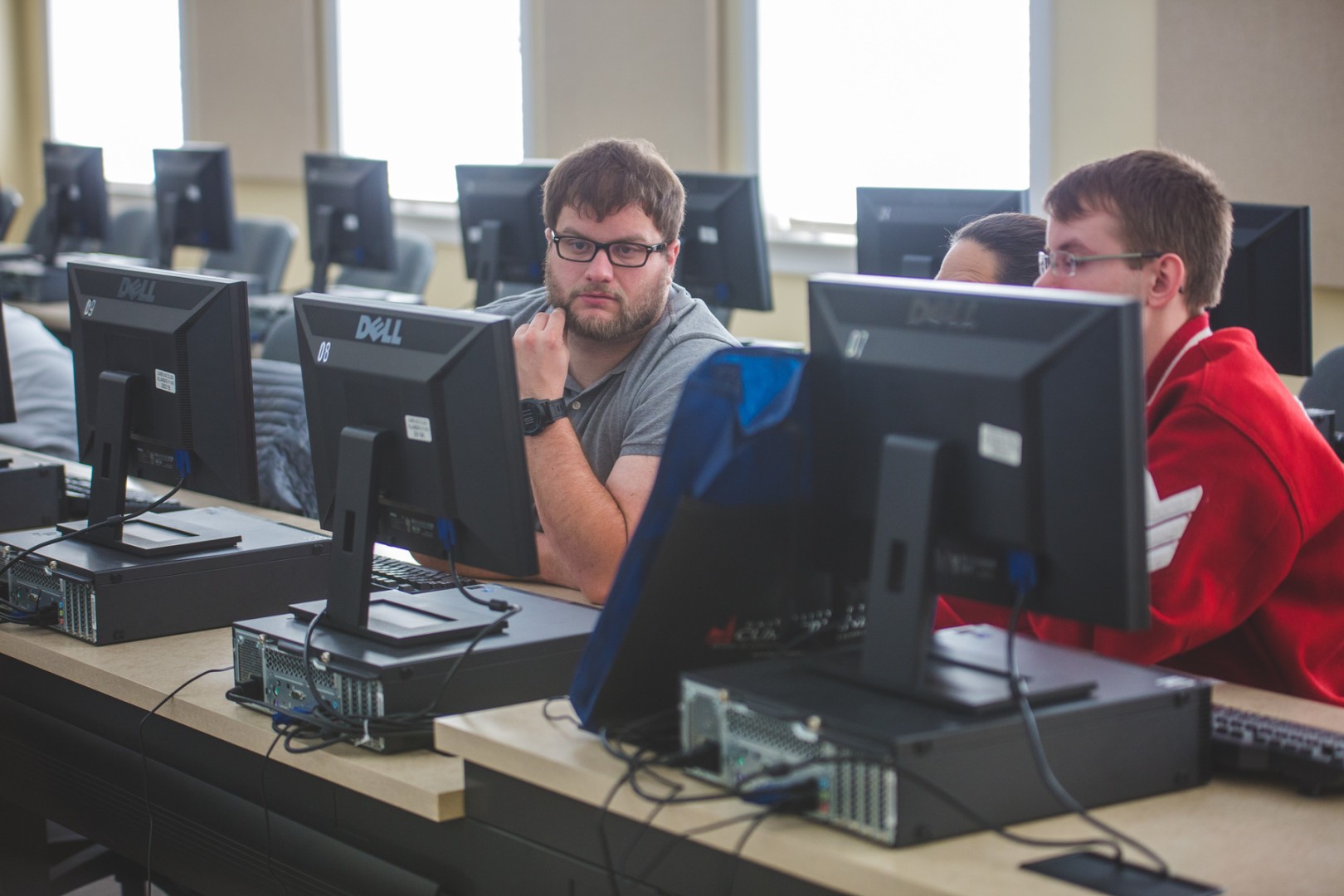 Two men in glasses sitting behind a row of computers.