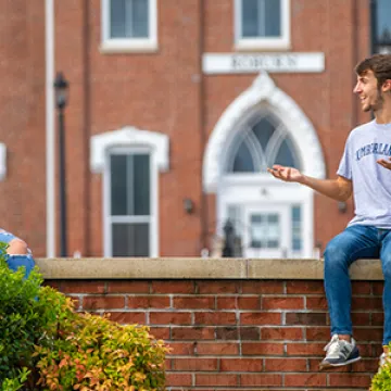 Two students sitting on a wall outside