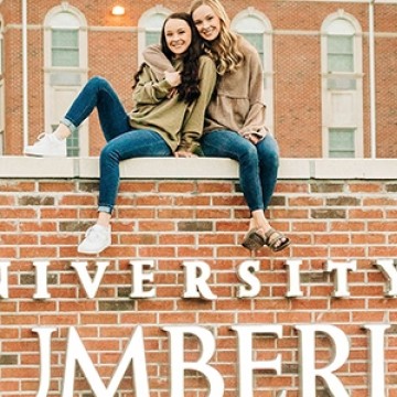 Two students posing for a picture seated on top of the University of the Cumberlands campus sign