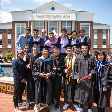Students wearing cap and gown with friends behind