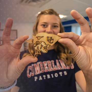 A student displays a woodcraft she made in the library maker space. 