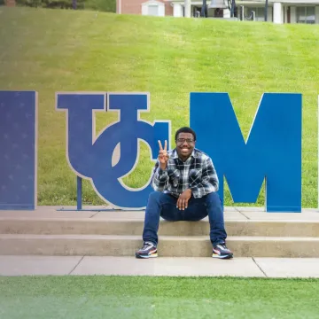A student sits by the Home sign on campus.