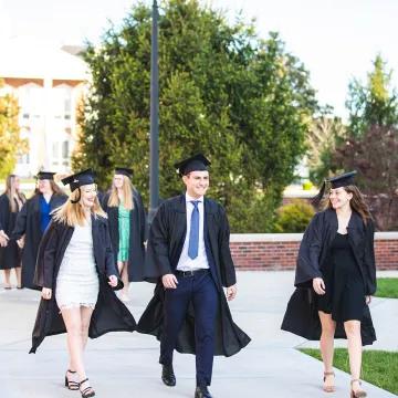 Graduates walk across the campus quad. 