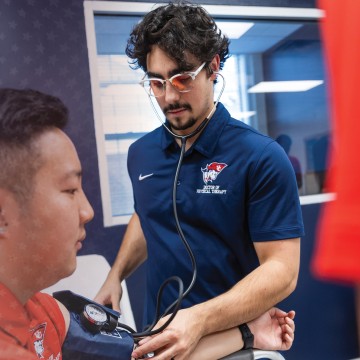 Two male DPT students check blood pressure during a clinical lab. 