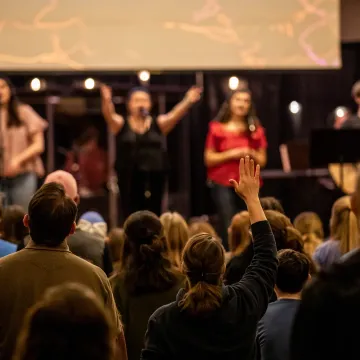 A group of students show praise during a worship event on campus while a band performs. 