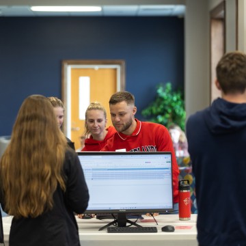 A group of students watch a male student demonstrate using AI during an info session in the student center. 