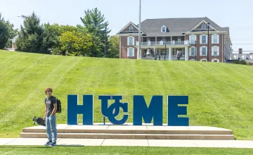 A student stands with a skateboard near Cumberlands HOME sign.