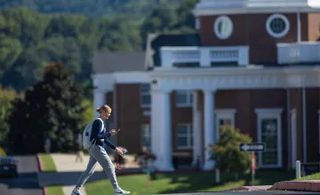 A student walks on campus in front of the science building. 