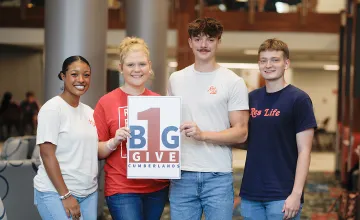 Students hold a sign promoting give day. 