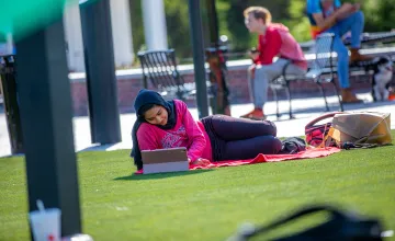 A female student relaxes on campus while using a computer. 