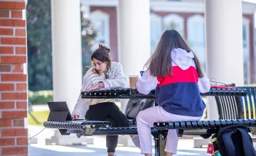 Two girls studying outside on a bench. 