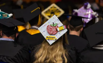 A decorated graduation hat with a teacher motif. 