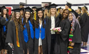 Six female graduates pose in cap and gown following the commencement service. 