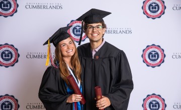 A female and male student pose with their diplomas after graduating. 