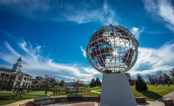 The sun peaks through a statue of the globe on campus. 
