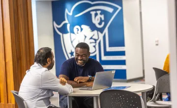Two male students chat at a table with their computer inside the Patriot Success Center. 