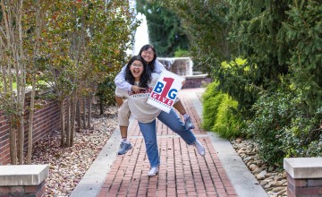 Two female students promote the One Big Give event while standing in front of the fountain. 