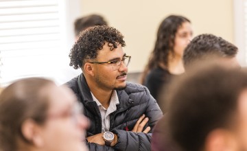 A male student with glasses listens to a speaker during the annual business forum. 