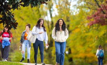 Two female students talk as they walk across campus on a fall morning. 
