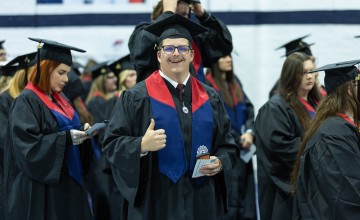 A male honors students gives a thumbs up just ahead of graduation services. 