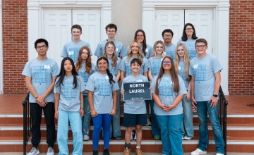 A group of high school students hold a sign with the school name on it at the annual math contest. 