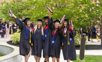 A group of five females in regalia celebrate with their diplomas following commencement services. 