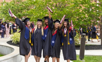 A group of five females in regalia celebrate with their diplomas following commencement services. 