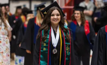 A female student walks with other graduates into the spring graduation ceremony. 