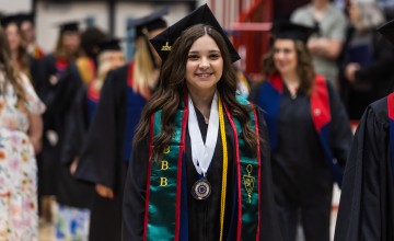 A female student walks with other graduates into the spring graduation ceremony. 