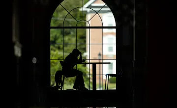 A student is studying in the campus grille but is silhouetted against the window behind her. 