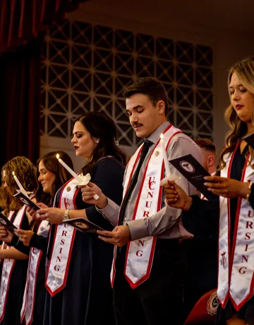 Nursing graduates hold candle and read their oath during a ceremony. 