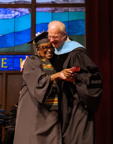 A female graduate hugs the university president after receiving her degree. 