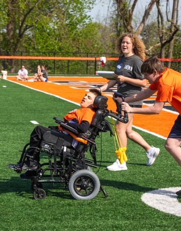 A male high school student, being coached by a Cumberlands student volunteer, pushes a child in a wheel chair during the 2026 Special Olympics.