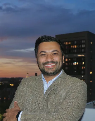 Dr. Aashis Luitel poses for a photo with a cityscape behind him. 