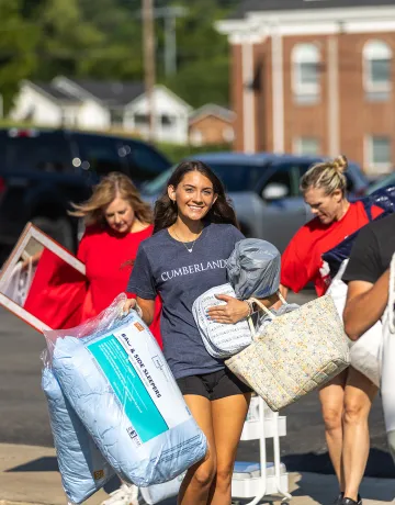 A freshmen female carries pillows from the parking lot to her dorm during move-in weekend. 