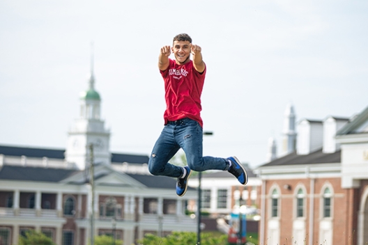 A student jumps on campus with dorms in the background