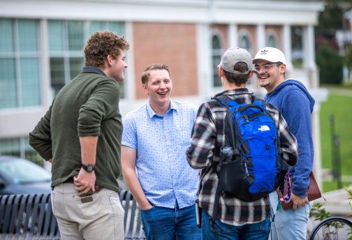 Four guys standing around talking on campus.