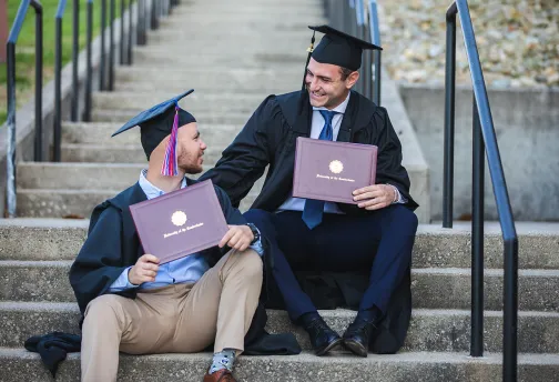 Two graduates display their diplomas