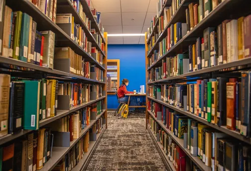 A student studying in the new library with books in the foreground. 