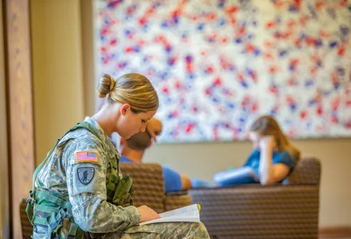Young woman in military uniform sitting and reading a book.