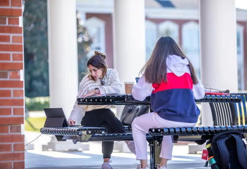 Two girls studying outside on a bench. 