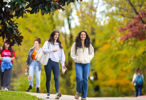 Two female students talk as they walk across campus on a fall morning. 