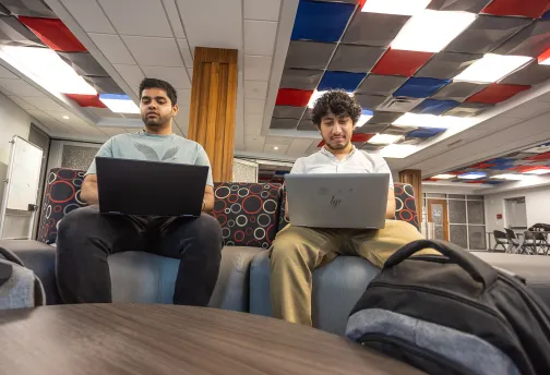 Two male executive students use their computers while in the student success center. 