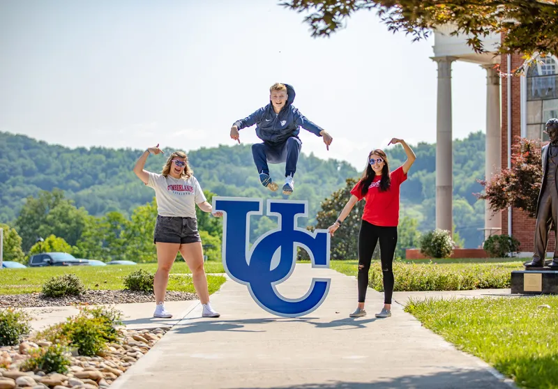 Students jump across the UC sign on campus. 