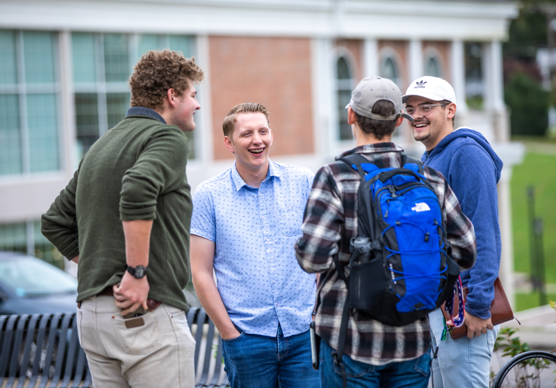 Four guys standing around talking on campus.