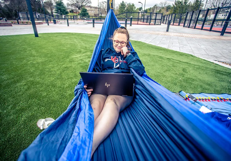 Girl using laptop sitting in hammock. 