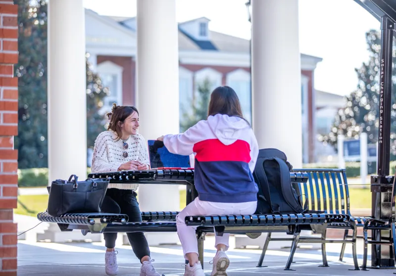 Two students seated at a table ouside