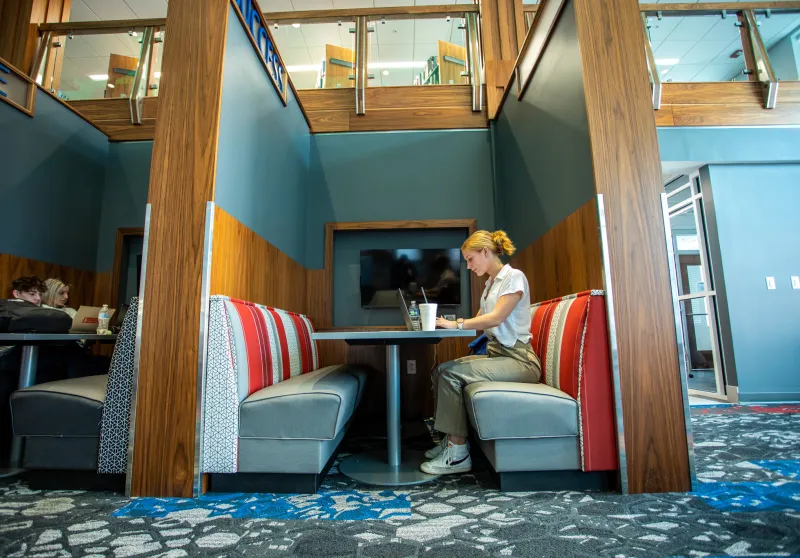 A student sitting in a booth and using a laptop