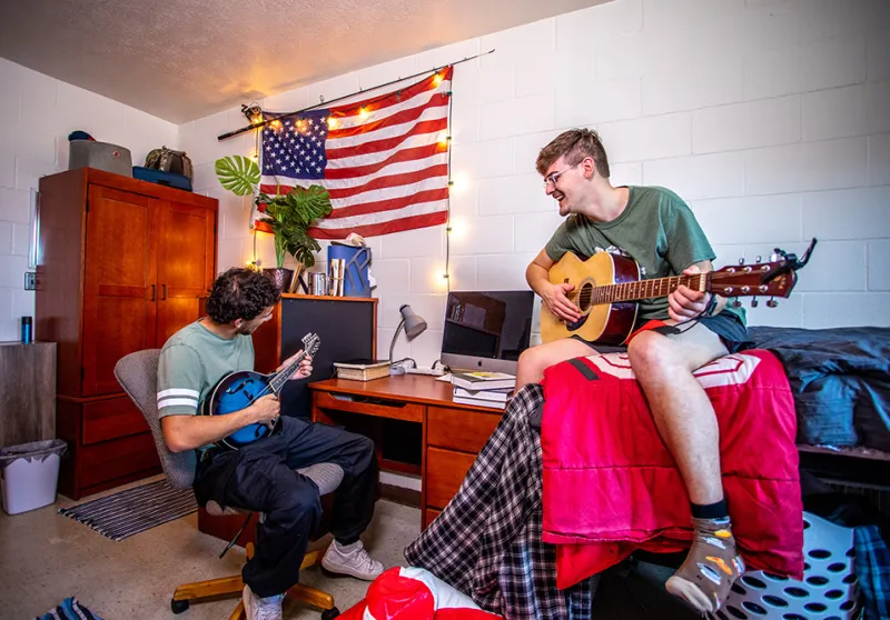 Two guys playing guitar in a dorm room